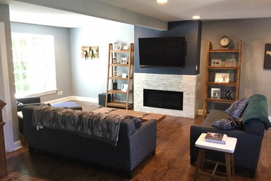 Example of a mid-sized transitional open concept medium tone wood floor and brown floor living room design in New York with blue walls, a standard fireplace, a stone fireplace and a wall-mounted tv