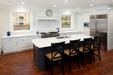 Design ideas for a large traditional galley kitchen in Sydney with with island, an undermount sink, raised-panel cabinets, white cabinets, marble benchtops, white splashback, ceramic splashback, stainless steel appliances, medium hardwood floors and brown floor.
