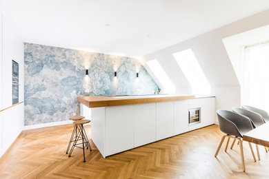 Große Skandinavische Wohnküche in L-Form mit flächenbündigen Schrankfronten, weißen Schränken, Arbeitsplatte aus Holz, hellem Holzboden, Kücheninsel, beigem Boden, beiger Arbeitsplatte, bunter Rückwand, Küchengeräten aus Edelstahl und Tapete in München