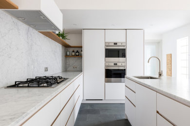 Photo of a medium sized contemporary grey and white kitchen/diner in London with a built-in sink, flat-panel cabinets, white cabinets, marble worktops, grey splashback, marble splashback, integrated appliances, slate flooring, an island, grey floors and grey worktops.
