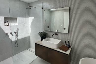 Design ideas for a mid-sized modern master bathroom in Sydney with brown cabinets, a freestanding tub, an open shower, a one-piece toilet, beige tile, porcelain tile, beige walls, porcelain floors, marble benchtops, beige floor, an open shower, beige benchtops, a single vanity, a floating vanity, beaded inset cabinets and a vessel sink.