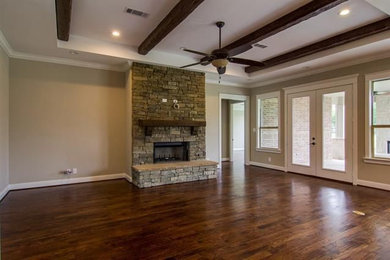 Inspiration for a large transitional open concept dark wood floor and brown floor family room remodel in Dallas with gray walls, a standard fireplace, a stone fireplace and a wall-mounted tv