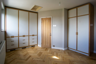 Minimalistisk inredning av ett mellanstort huvudsovrum, med grå väggar och ljust trägolv