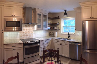 Photo of a country kitchen in Cincinnati with a double-bowl sink, raised-panel cabinets, beige cabinets, granite benchtops, white splashback, terra-cotta splashback, stainless steel appliances and brown floor.