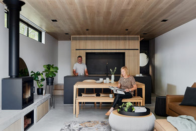 This is an example of a small industrial open concept living room in Melbourne with white walls, concrete floors, a wood stove, a concrete fireplace surround, a wall-mounted tv, grey floor and wood.
