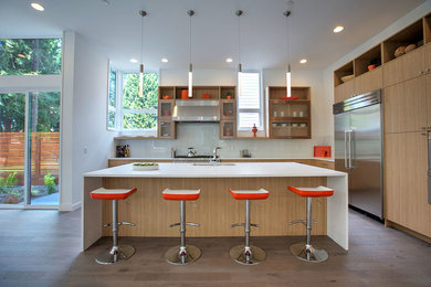This is an example of a large modern l-shaped open plan kitchen in Seattle with an undermount sink, flat-panel cabinets, light wood cabinets, quartz benchtops, white splashback, glass tile splashback, stainless steel appliances, medium hardwood floors, with island, brown floor and white benchtop.