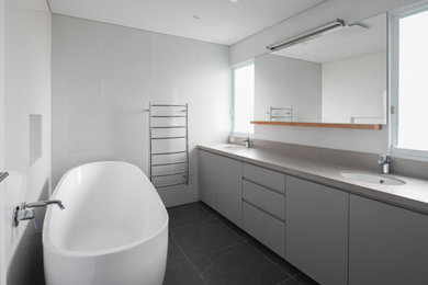 Inspiration for a mid-sized contemporary kids bathroom in Sydney with beaded inset cabinets, grey cabinets, a freestanding tub, a corner shower, a one-piece toilet, ceramic tile, grey walls, ceramic floors, an undermount sink, engineered quartz benchtops, grey floor, a hinged shower door, grey benchtops, a double vanity and a built-in vanity.