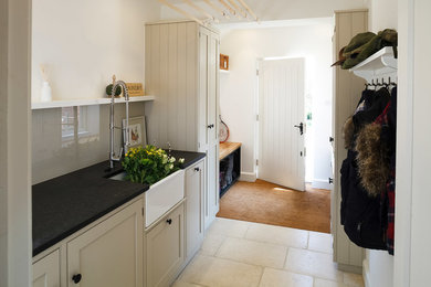 Traditional laundry room in Cambridgeshire with a farmhouse sink, shaker cabinets, granite benchtops, white walls and limestone floors.