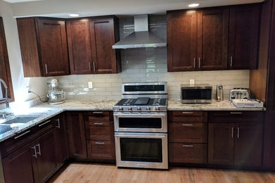 Example of a transitional light wood floor kitchen design in Seattle with an undermount sink, flat-panel cabinets, dark wood cabinets, granite countertops, beige backsplash, glass tile backsplash, stainless steel appliances and multicolored countertops