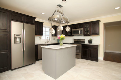 Transitional l-shaped kitchen photo in New York with raised-panel cabinets, dark wood cabinets, granite countertops, white backsplash, glass sheet backsplash, stainless steel appliances and an island
