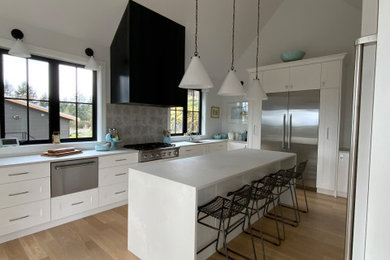 Example of a large transitional u-shaped light wood floor, white floor and vaulted ceiling eat-in kitchen design with an undermount sink, shaker cabinets, white cabinets, quartz countertops, gray backsplash, porcelain backsplash, stainless steel appliances, an island and gray countertops