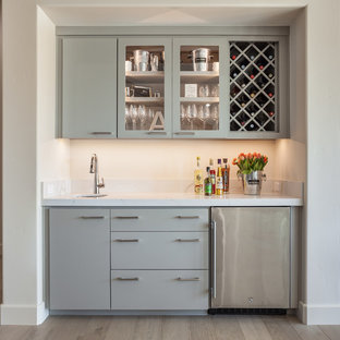 サクラメントの中サイズのトランジショナルスタイルのおしゃれなウェットバー (アンダーカウンターシンク、フラットパネル扉のキャビネット、グレーのキャビネット、クオーツストーンカウンター、淡色無垢フローリング、ベージュの床、白いキッチンカウンター) の写真