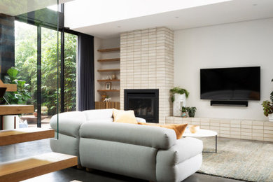 Cette photo montre un grand salon tendance ouvert avec un mur blanc, sol en béton ciré, une cheminée standard, un manteau de cheminée en brique, un téléviseur fixé au mur et un sol gris.