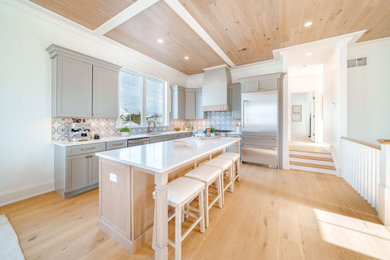 Example of a beach style l-shaped light wood floor, beige floor and wood ceiling kitchen design in Philadelphia with an undermount sink, shaker cabinets, gray cabinets, blue backsplash, stainless steel appliances, an island and white countertops
