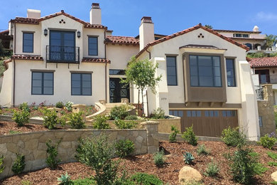 Example of a large tuscan beige three-story stucco house exterior design in Santa Barbara with a clipped gable roof and a tile roof