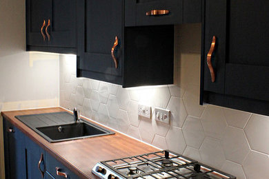 Small modern l-shaped kitchen/diner in Cardiff with a single-bowl sink, shaker cabinets, blue cabinets, laminate countertops, white splashback, ceramic splashback, stainless steel appliances, laminate floors, a breakfast bar, beige floors, red worktops and a feature wall.