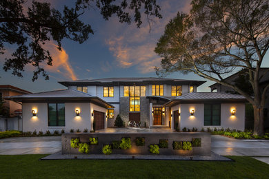 Large trendy beige two-story stucco house exterior photo in Tampa with a hip roof and a metal roof