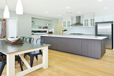 This is an example of a large modern l-shaped open plan kitchen in Central Coast with an undermount sink, glass-front cabinets, white cabinets, marble benchtops, white splashback, glass sheet splashback, stainless steel appliances, laminate floors and with island.