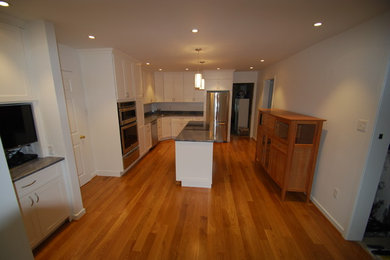 Inspiration for a mid-sized timeless l-shaped medium tone wood floor and brown floor eat-in kitchen remodel in Philadelphia with white cabinets, white backsplash, stainless steel appliances, an island, an undermount sink and shaker cabinets