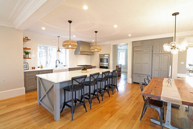 Large country l-shaped eat-in kitchen in Boston with a farmhouse sink, beaded inset cabinets, grey cabinets, quartz benchtops, white splashback, ceramic splashback, stainless steel appliances, medium hardwood floors, with island, multi-coloured floor and white benchtop.
