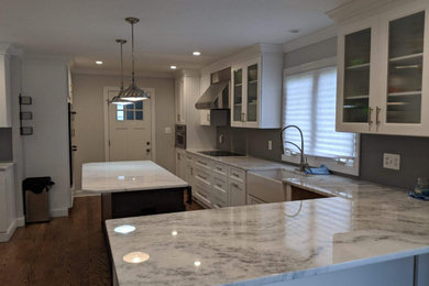 Photo of a large transitional u-shaped eat-in kitchen in New York with a farmhouse sink, recessed-panel cabinets, white cabinets, quartzite benchtops, grey splashback, glass tile splashback, stainless steel appliances, medium hardwood floors, with island, brown floor and multi-coloured benchtop.