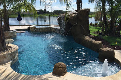 Design ideas for a mid-sized tropical backyard custom-shaped lap pool in Orlando with a hot tub and natural stone pavers.