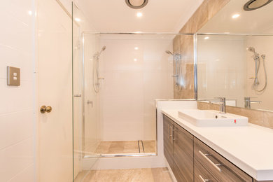Design ideas for a mid-sized contemporary master bathroom in Perth with flat-panel cabinets, brown cabinets, an alcove shower, white tile, ceramic tile, ceramic floors, a vessel sink, engineered quartz benchtops, beige floor, a hinged shower door and white benchtops.