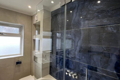 Photo of a small modern family bathroom in London with flat-panel cabinets, beige cabinets, a corner bath, a shower/bath combination, a wall mounted toilet, blue tiles, porcelain tiles, beige walls, porcelain flooring, an integrated sink, beige floors, a single sink and a floating vanity unit.