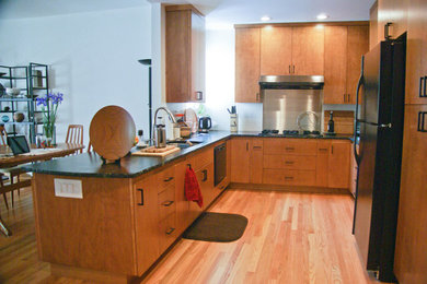 Small contemporary u-shaped eat-in kitchen in Sacramento with a drop-in sink, flat-panel cabinets, medium wood cabinets, soapstone benchtops, black appliances, medium hardwood floors and a peninsula.