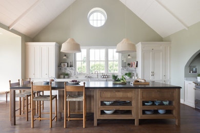 Large traditional l-shaped kitchen in London with a belfast sink, shaker cabinets, quartz worktops, engineered quartz splashback, integrated appliances, dark hardwood flooring, an island, brown floors, a vaulted ceiling, a chimney breast, white cabinets, white splashback and white worktops.