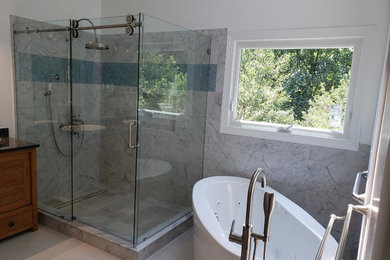 Inspiration for a large contemporary master bathroom in Raleigh with furniture-like cabinets, medium wood cabinets, a freestanding tub, a corner shower, a two-piece toilet, gray tile, white tile, marble, white walls, ceramic floors, a vessel sink, granite benchtops, white floor, a hinged shower door and black benchtops.