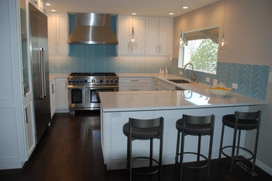 This is an example of a small beach style u-shaped eat-in kitchen in Denver with an undermount sink, white cabinets, quartz benchtops, blue splashback, glass tile splashback, stainless steel appliances, dark hardwood floors, a peninsula, brown floor and white benchtop.