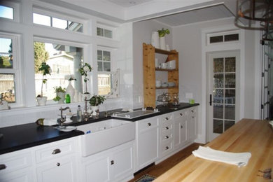 Example of a mid-sized cottage l-shaped brick floor eat-in kitchen design in San Diego with a farmhouse sink, shaker cabinets, white cabinets, soapstone countertops, white backsplash, subway tile backsplash and an island