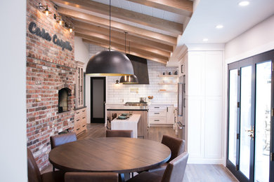Eat-in kitchen - large cottage l-shaped medium tone wood floor and brown floor eat-in kitchen idea in San Francisco with a farmhouse sink, shaker cabinets, white cabinets, quartz countertops, white backsplash, subway tile backsplash, stainless steel appliances and an island