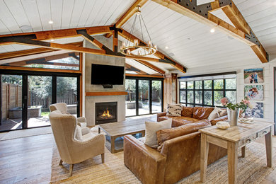 This is an example of a country family room in San Francisco with white walls, light hardwood floors, a standard fireplace and a wall-mounted tv.