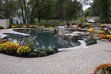 This is an example of a mid-sized traditional backyard custom-shaped natural pool in New York with a water slide and concrete pavers.