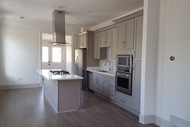 Inspiration for a mid-sized transitional single-wall medium tone wood floor eat-in kitchen remodel in New Orleans with an undermount sink, shaker cabinets, gray cabinets, solid surface countertops, white backsplash, mosaic tile backsplash, stainless steel appliances and an island