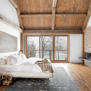 Cette photo montre une très grande chambre parentale tendance avec un mur blanc, un sol en bois brun, une cheminée standard et un manteau de cheminée en métal.
