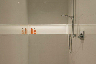 Photo of a large modern master bathroom in Dusseldorf with white cabinets, a freestanding tub, an open shower, a two-piece toilet, white walls, an integrated sink, glass benchtops, beige floor, an open shower, white benchtops, white tile, flat-panel cabinets, ceramic tile, limestone floors, a single vanity, a floating vanity, recessed and decorative wall panelling.