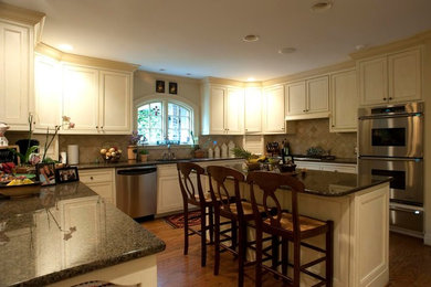 Mid-sized elegant u-shaped medium tone wood floor and brown floor eat-in kitchen photo in Birmingham with an undermount sink, raised-panel cabinets, white cabinets, beige backsplash, stainless steel appliances and an island