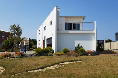 Aménagement d'une façade de maison blanche contemporaine en panneau de béton fibré à un étage et de taille moyenne avec un toit à croupette, un toit en métal et un toit blanc.