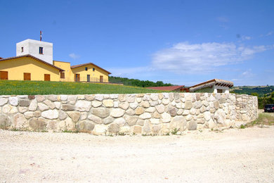 Foto di un grande vialetto d'ingresso country esposto in pieno sole davanti casa in estate con un muro di contenimento e sassi di fiume