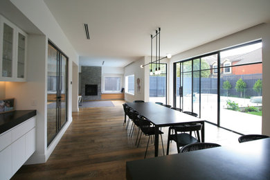 Photo of a large contemporary open plan dining in Melbourne with white walls, medium hardwood floors, a standard fireplace and a brick fireplace surround.