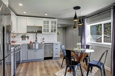 Open concept kitchen - small contemporary l-shaped laminate floor and brown floor open concept kitchen idea in Seattle with a farmhouse sink, shaker cabinets, gray cabinets, quartz countertops, multicolored backsplash, stone slab backsplash, stainless steel appliances, white countertops and no island