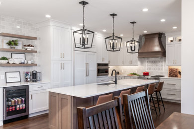 This is an example of a large country l-shaped eat-in kitchen in St Louis with an undermount sink, shaker cabinets, white cabinets, quartz benchtops, grey splashback, porcelain splashback, panelled appliances, medium hardwood floors, with island, brown floor and white benchtop.