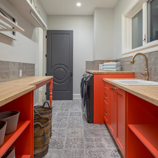Coastal galley separated utility room in Vancouver with a built-in sink, shaker cabinets, orange cabinets, wood worktops, grey walls, a side by side washer and dryer, grey floors and beige worktops.