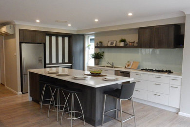 Photo of a mid-sized contemporary kitchen in Sydney with a double-bowl sink, flat-panel cabinets, dark wood cabinets, solid surface benchtops, glass sheet splashback, stainless steel appliances, vinyl floors and with island.