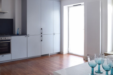 Inspiration for a medium sized modern galley kitchen/diner in London with an integrated sink, flat-panel cabinets, grey cabinets, grey splashback, stainless steel appliances, medium hardwood flooring, no island, brown floors and grey worktops.