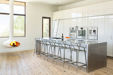 Inspiration for a large contemporary single-wall medium tone wood floor open concept kitchen remodel in Denver with an integrated sink, flat-panel cabinets, white cabinets, stainless steel countertops, stainless steel appliances and an island