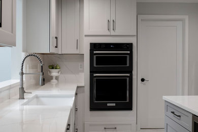 デトロイトにある高級な広いトランジショナルスタイルのおしゃれなキッチン (アンダーカウンターシンク、シェーカースタイル扉のキャビネット、グレーのキャビネット、クオーツストーンカウンター、白いキッチンパネル、クオーツストーンのキッチンパネル、シルバーの調理設備、磁器タイルの床、白い床、白いキッチンカウンター) の写真